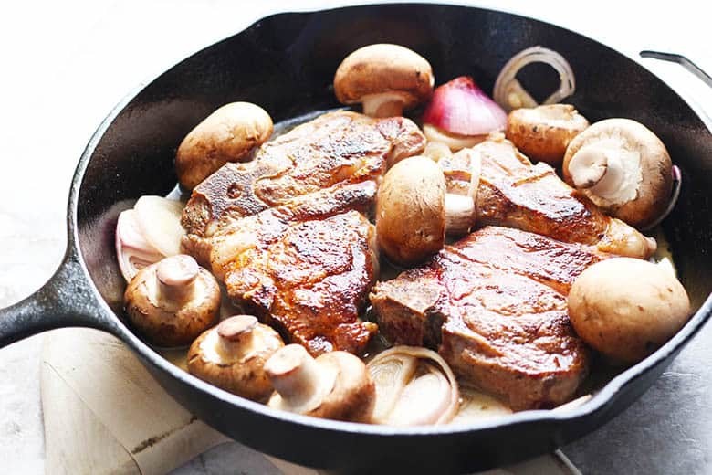 Lamb chops cooked in a skillet with mushrooms.
