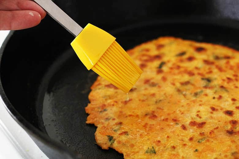 Brushing butter on a paratha in a skillet.