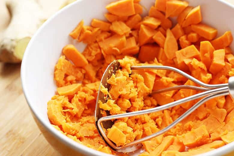 Cooked sweet potatoes being mashed in a bowl.