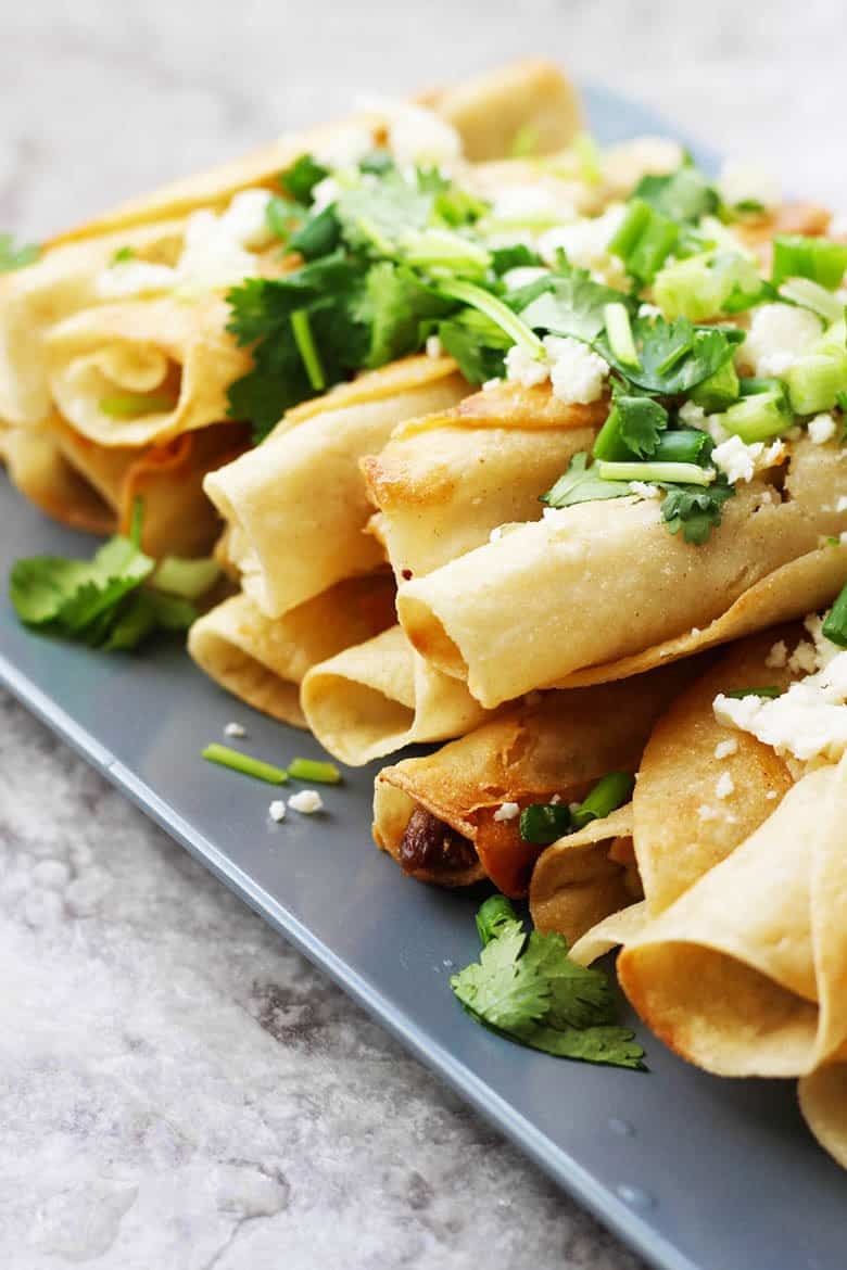 A plate of Chicken Mexican Flautas garnished with cilantro and cheese.