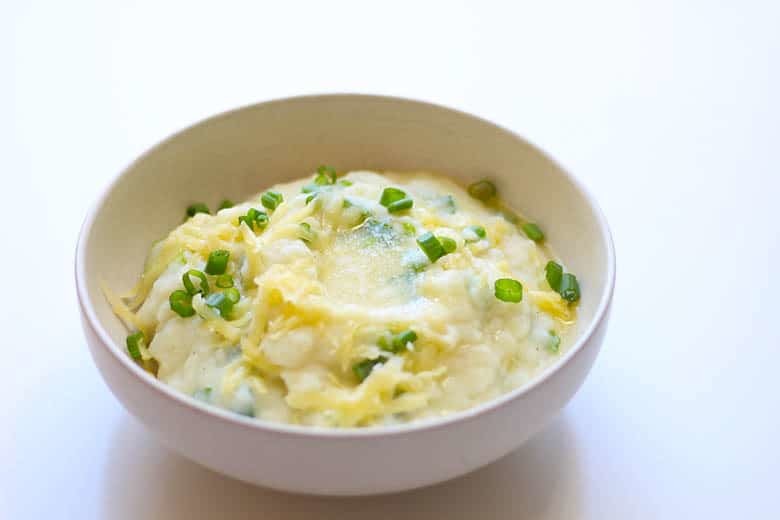 A bowl of hearty Irish Champ, garnished with cheese and more scallions.