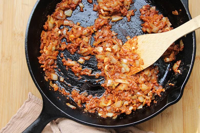 A cast iron skillet with fried chorizo sausage and diced onion.