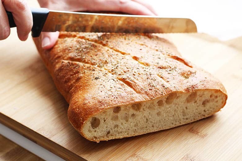 Ciabatta bread being cut in half on a bread board.