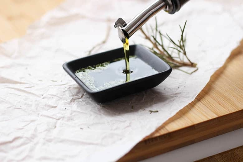 Olive oil being poured over rosemary.