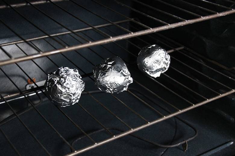 Three potatoes wrapped in foil in oven.