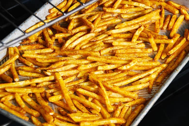 Cooked fries in an oven on a baking sheet.