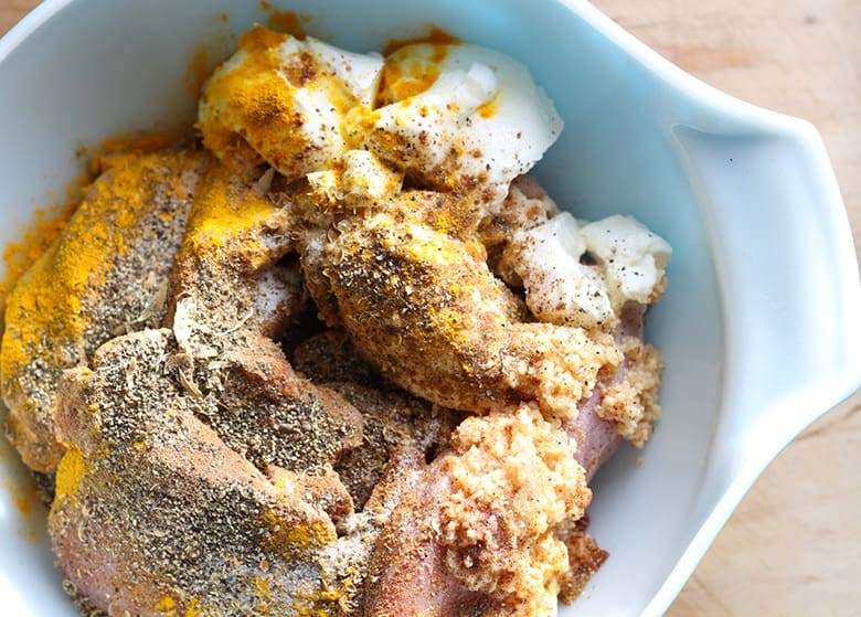 Raw chicken in a bowl covered in yogurt and spices.
