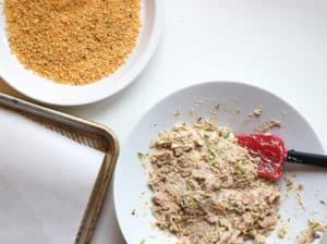 Mackerel mix in a bowl next to a plate with bread crumbs and a rimmed baking sheet lined with paper.