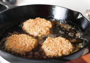 Three fish cakes in a cast iron skillet with oil.