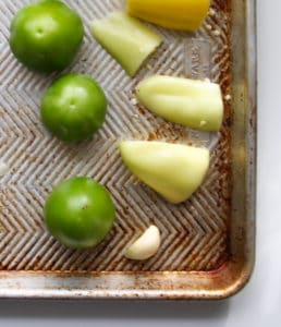 Tomatillos, peppers and garlic on a baking sheet.