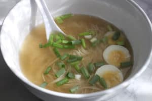 A bowl of noodle soup with scallions and hard boiled eggs.