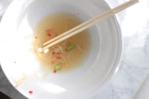 A mostly empty bowl of soup with chopsticks.