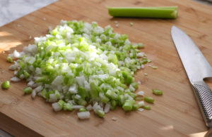 Chopped onion and celery on cutting board.