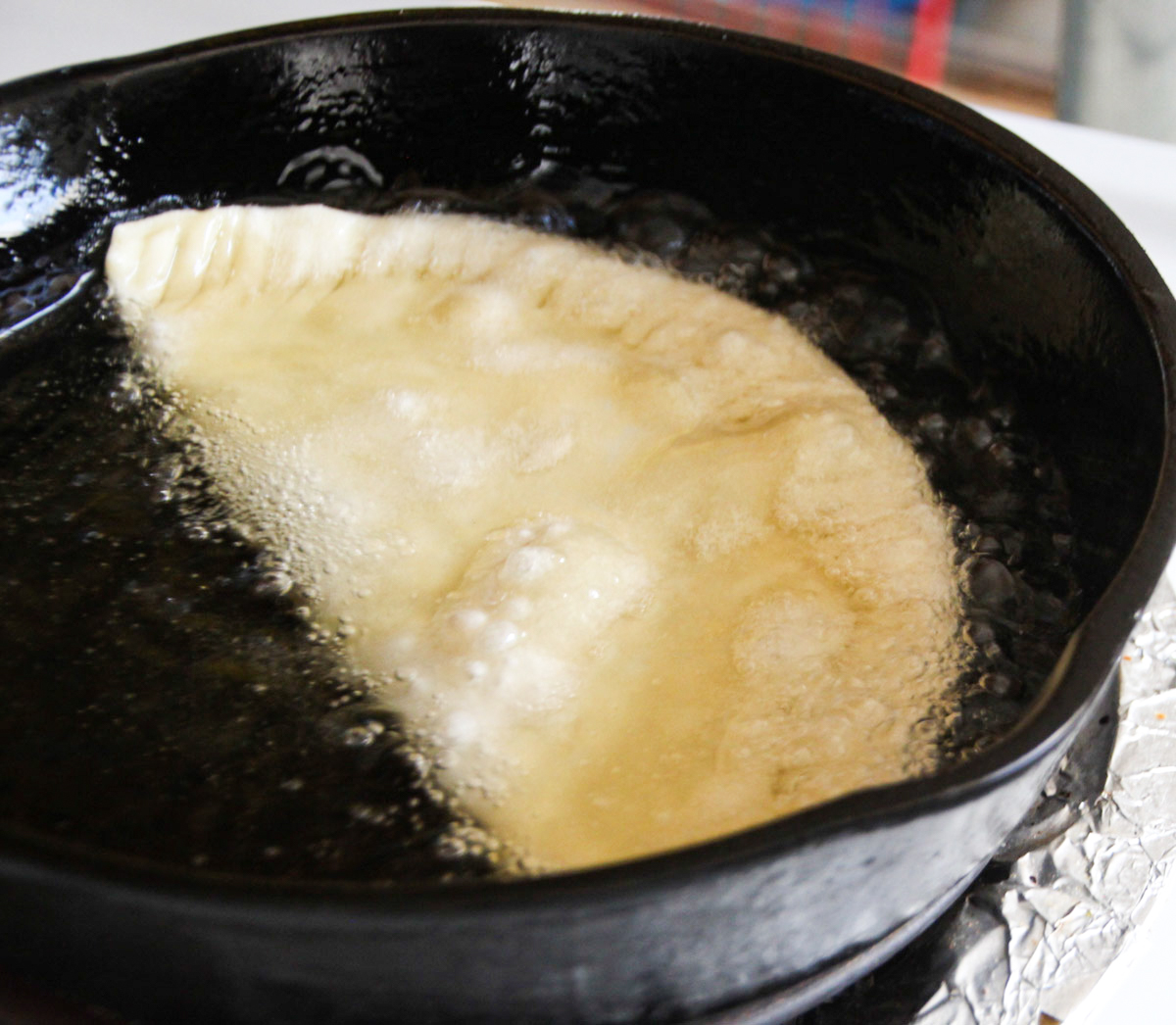 Chebureki pie deep frying in skillet.