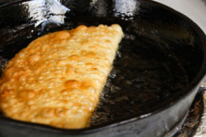 Chebureki pie deep frying in skillet.